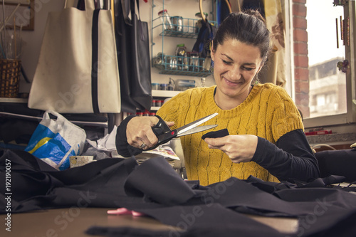 Young woman, a tailor seamstress, cutting a piece of black cloth in her workshop
