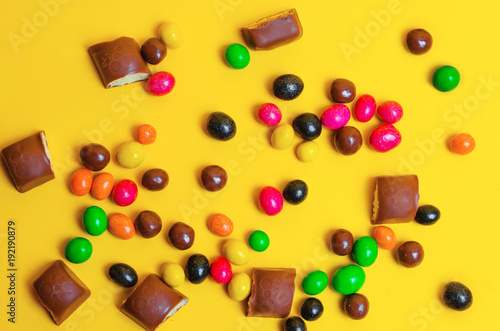 chocolate bars, colorful candies, sweets on a yellow background, top view