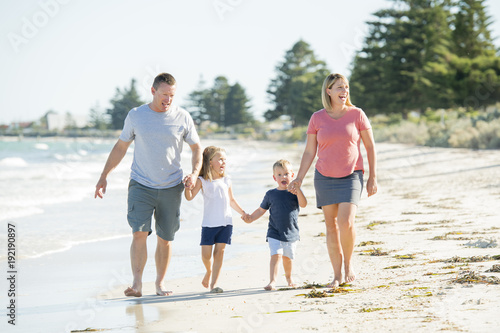 young happy and beautiful family mother father holding hand of son and daughter walking joyful on the beach enjoying Summer holidays