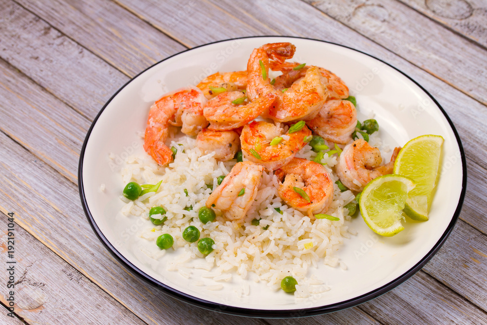 Shrimps with ginger rice and green peas, lime on white plate on wooden background Shrimps with ginger rice and green peas, lime on white plate on wooden background