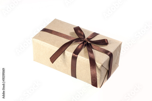 Gift box or present wrapped in brown craft paper and decorated satin ribbon knotted on a bow isolated on white background