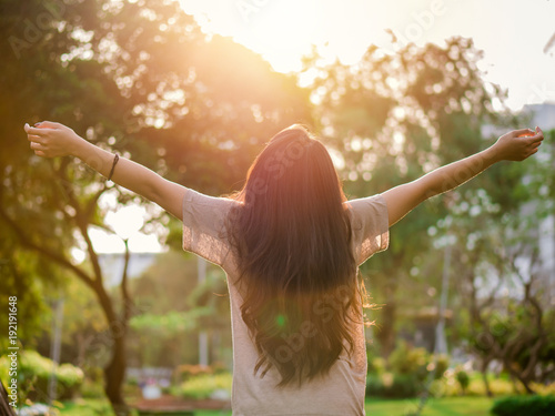 Young asian woman arms raised enjoying the fresh air in green forest  at public park.