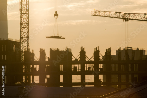 Construction side at sunset - workers, cranes - unfinished building
