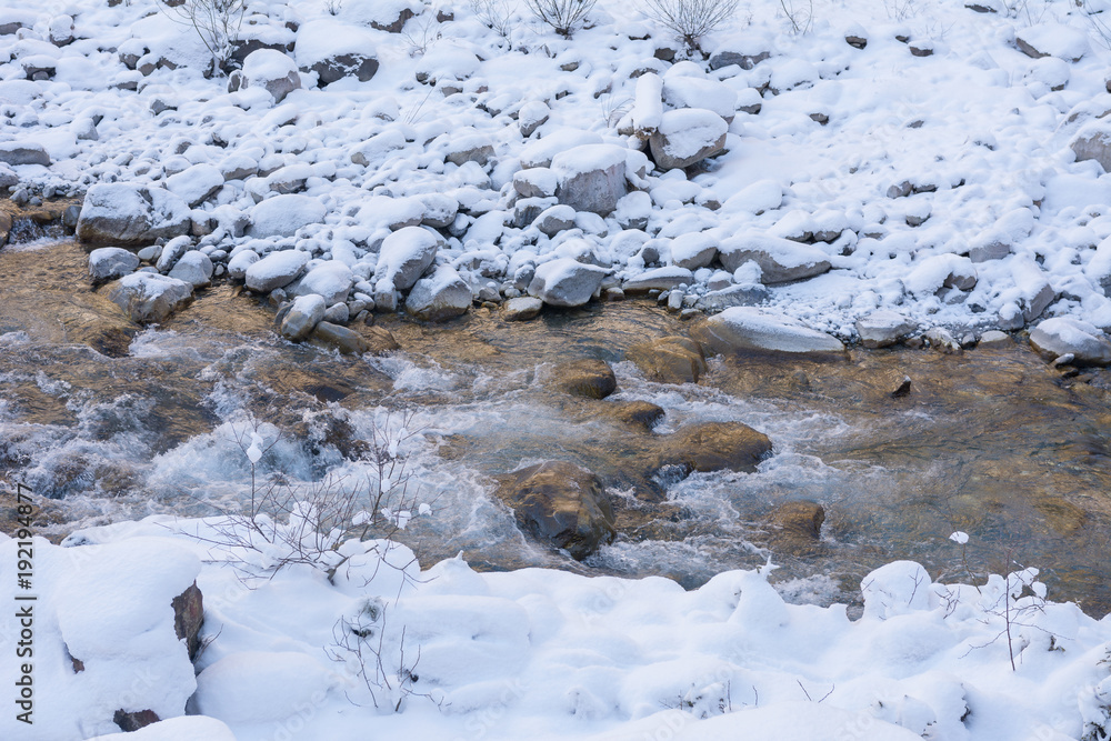 Fluss durch den verschneiten weissen Wald mit Steinen