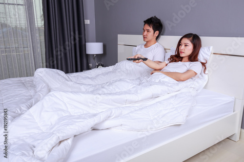 young couple lying on a bed with remote control and watching television in bedroom