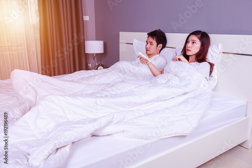 young couple lying on a bed with remote control of air conditioner in bedroom