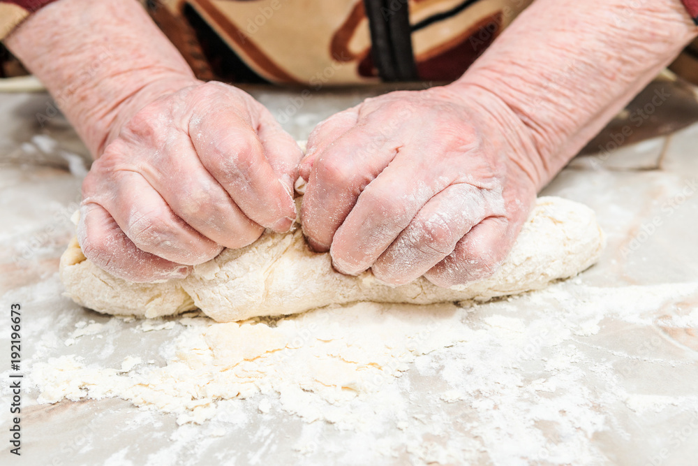 Female old hands knead the dough on a table, close-up