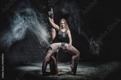 Two girls dance with flour on black background