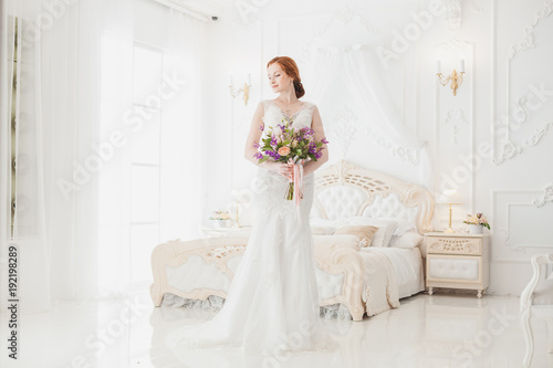 Bride in the wedding dress is standing in the royal bedroom, she is waiting for her fiance.