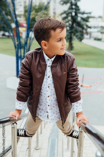 Teenager boy is waiting for the stairs at the railing. Fashionable kid in stylish city clothes.
