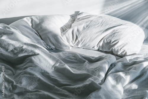фотографія white crumpled bed with pillow and blnaket