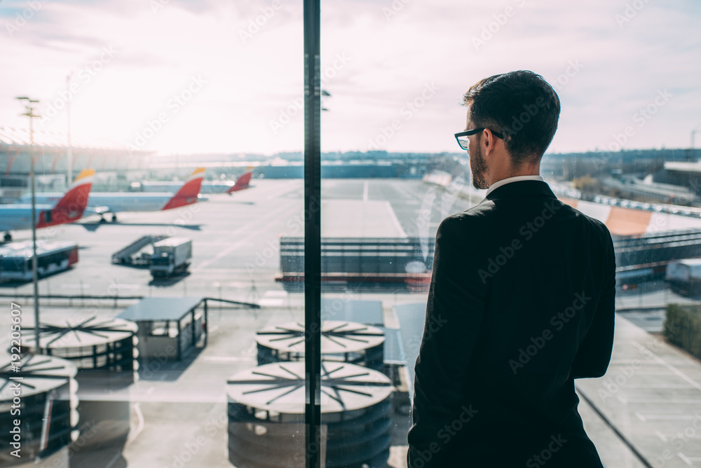 Back of a young business man standing with the suitcase at the airport waiting for the flight . Back of a young business man standing with the suitcase at the airport waiting for the flight .