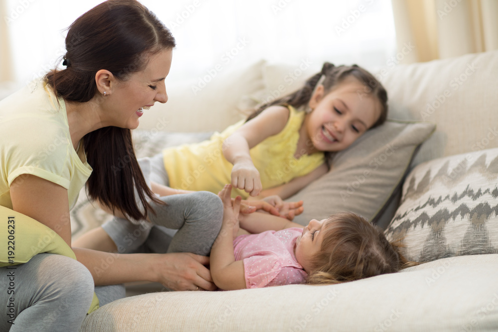 Smiling kids and their mom having a fun pastime on sofa in living room at home Smiling kids and their mom having a fun pastime on sofa in living room at home
