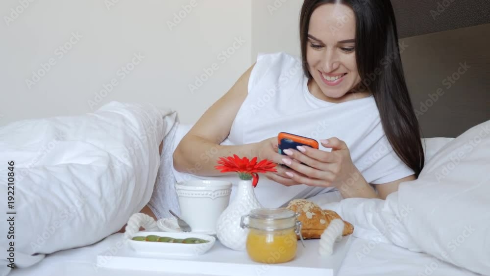 Brunette with coffee in bed using smartphone Brunette with coffee in bed using smartphone