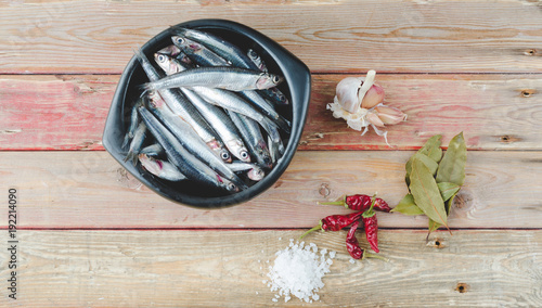 Fresh anchovies in black bowl on wooden background. Top view.