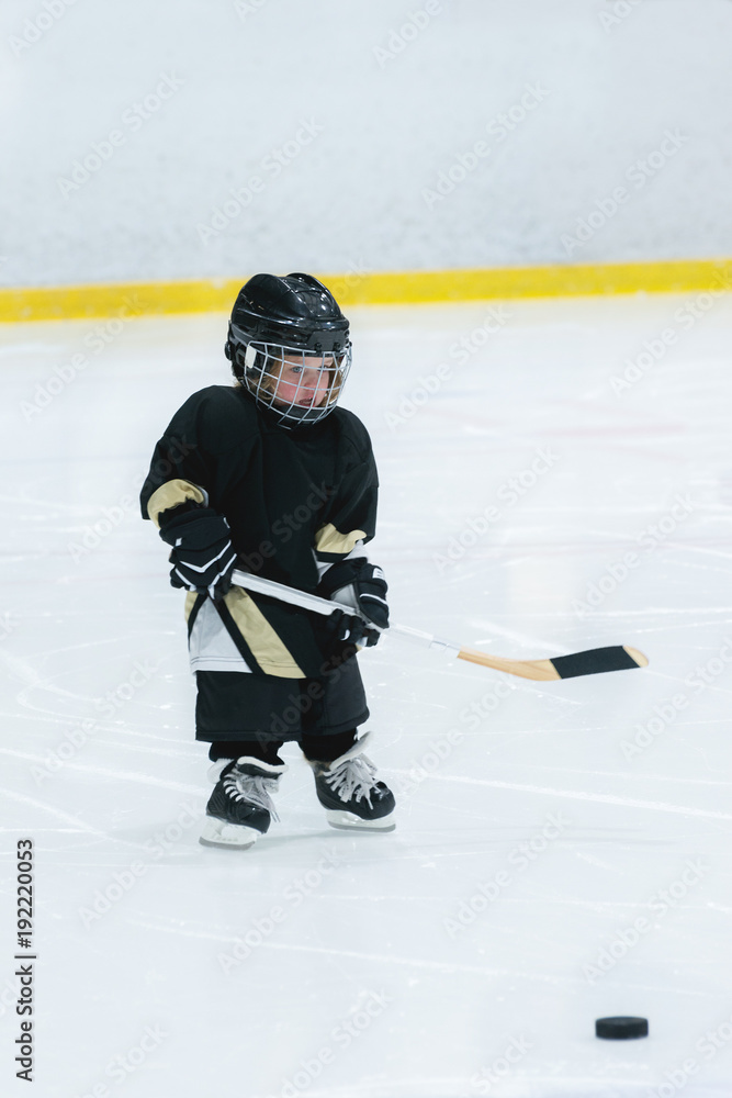 Obraz premium Little cute blond girl plays hockey in full equipment on the ice arena