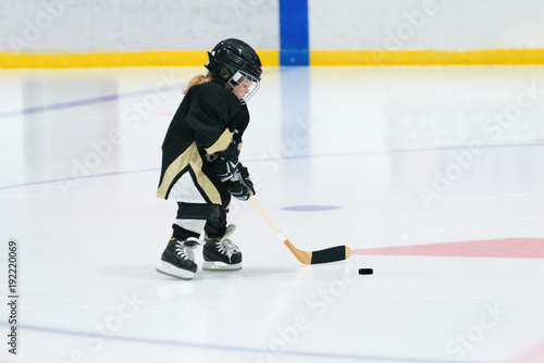 Little cute blond girl plays hockey in full equipment on the stadium