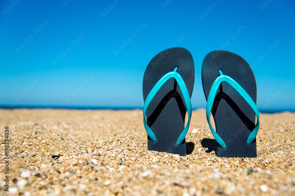 blue flip-flops on the sand - a concept for summer vacation, travel and leisure