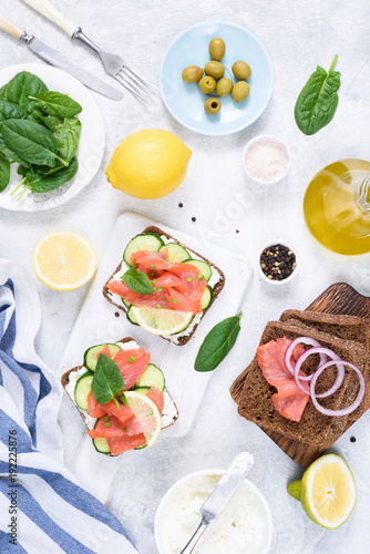 Toast sandwiches with salmon, cream cheese, olives and cucumber on white table. Top view. Dinner table