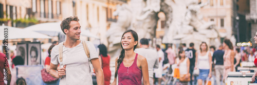 Rome travel young couple tourists walking in city streets on Navona Square sightseeing in Italy. Asian woman talking with Caucasian man happy, students lifestyle. Banner panorama landscape background.