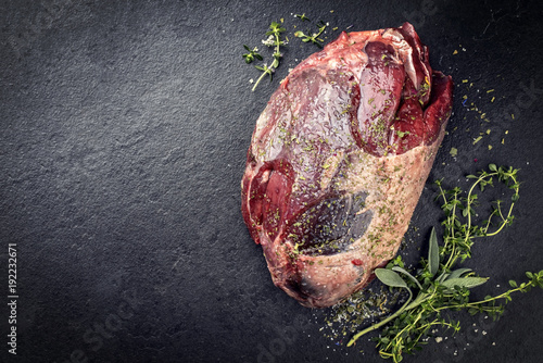 Photo Raw dry aged haunch of venison as with herbs as close-up on a slate slab with co