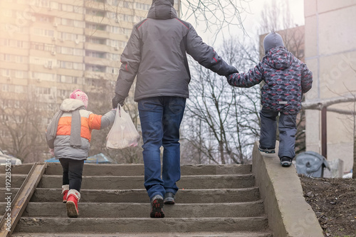 Fototapeta Naklejka Na Ścianę i Meble -  Rear view of father and two kids holding hands while walking on the street