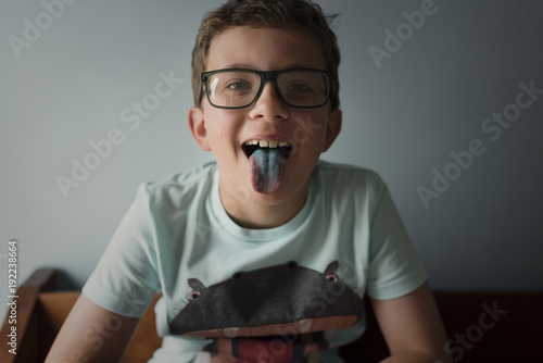 Portrait of playful boy sticking out tongue against wall at home