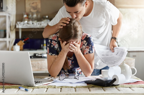 Fotografia Sad woman covers face with hands, feels desperate and embarrased, recives bank invoice or bill, sit together with partnet at kitchen table, don`t see way out in difficult financial situation