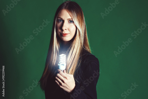 Serious young business woman holding a light bulb on a green background. Concept of ideas and symbolization