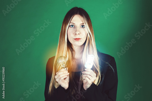 Serious pretty business woman holding a light bulb on a green background. Close-up of a hands model. Old bulb against a new bulb © Pavel