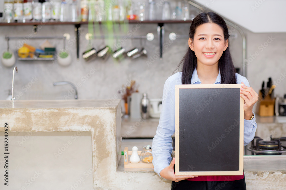 Portrait of beautiful young barista, asian woman is a employee standing holding chalkboard in counter coffee shop, service concept. Portrait of beautiful young barista, asian woman is a employee standing holding chalkboard in counter coffee shop, service concept.