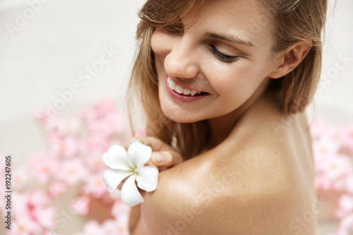 Young pleasant looking female model enjoys hot bath with beutiful flowers, has spa treatments for skin rejuvenation, shows her naked perfect body, cares of appearance. Beauty and care concept