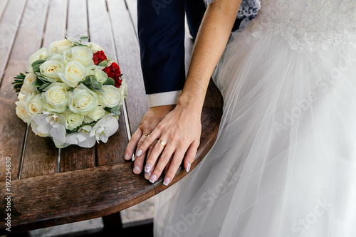 Hands of bride and groom with rings and bouquet of white roses and orchids on the table