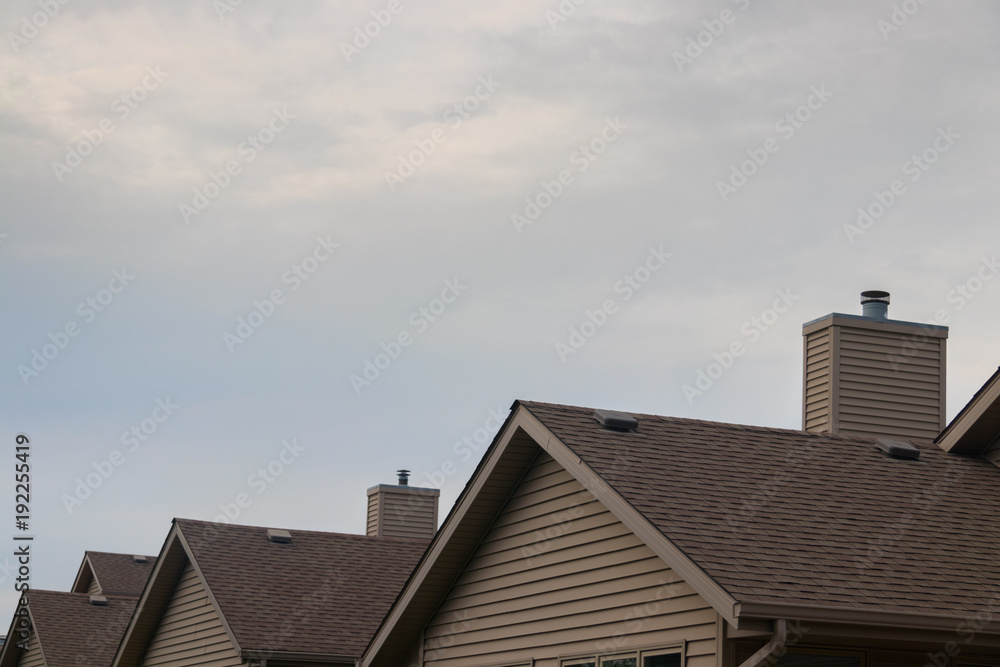 Detail of plain, beige suburban rooftops with cloudy sky.
