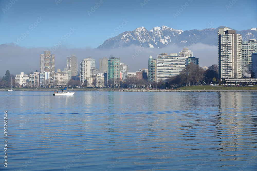 Fototapeta premium English Bay, Coast Mountains, Sailboat. A sailboat crosses English Bay. In the background are the snowcapped North Shore Mountains. Vancouver, British Columbia, Canada.