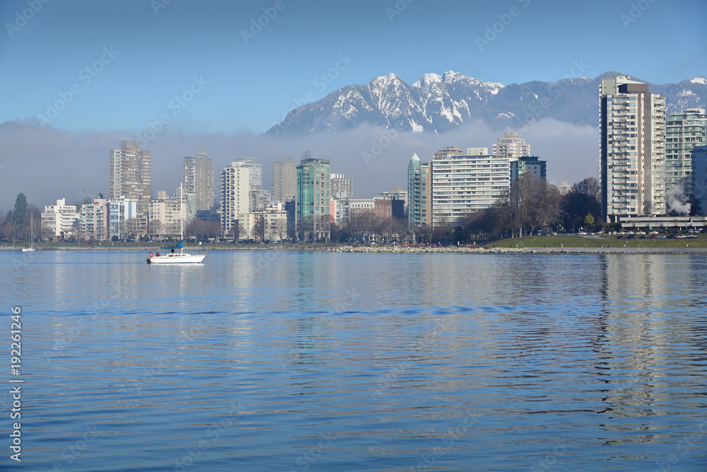 English Bay, Coast Mountains, Sailboat. A sailboat crosses English Bay. In the background are the snowcapped North Shore Mountains. Vancouver, British Columbia, Canada.

