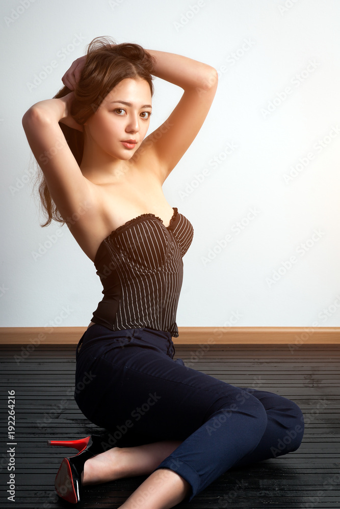 Asian young woman in black top and classic black pants posing and sitting on a black wooden floor against a white wall background Asian young woman in black top and classic black pants posing and sitting on a black wooden floor against a white wall background