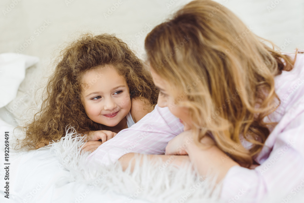 happy mother and curly daughter lying on sheep skin blanket and looking at each other happy mother and curly daughter lying on sheep skin blanket and looking at each other