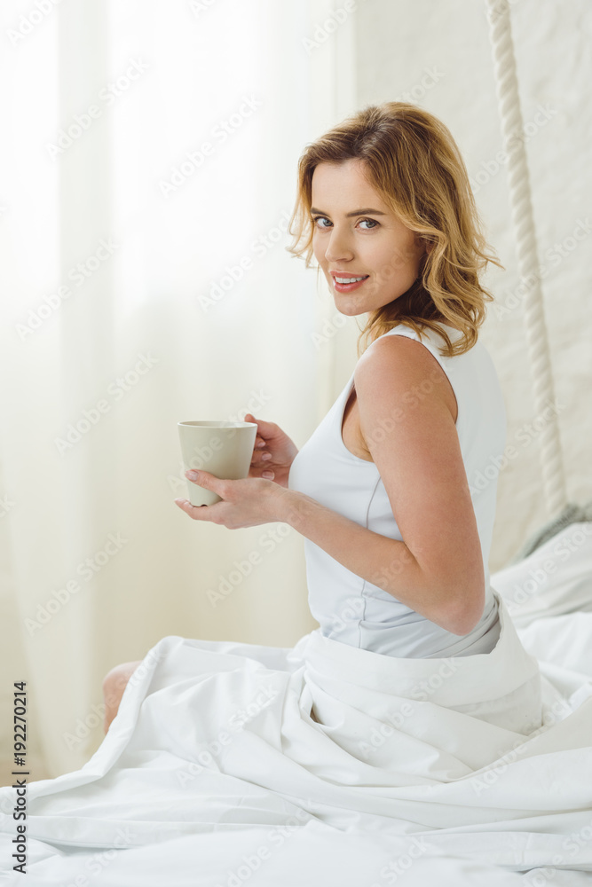 smiling beautiful woman with cup of coffee sitting on bed in the morning smiling beautiful woman with cup of coffee sitting on bed in the morning