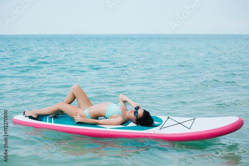 young slim girl lying on paddle board on sea at tropical resort