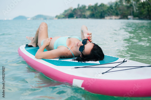 beautiful woman lying on paddle board on sea at tropical resort