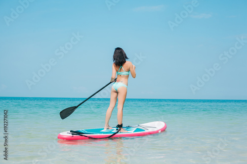 back view of girl on stand up paddle board on sea at tropical resort