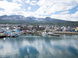 The town and docks of Ushuaia Argentina photographed from the bay. The cloudy sky is reflected in the water.