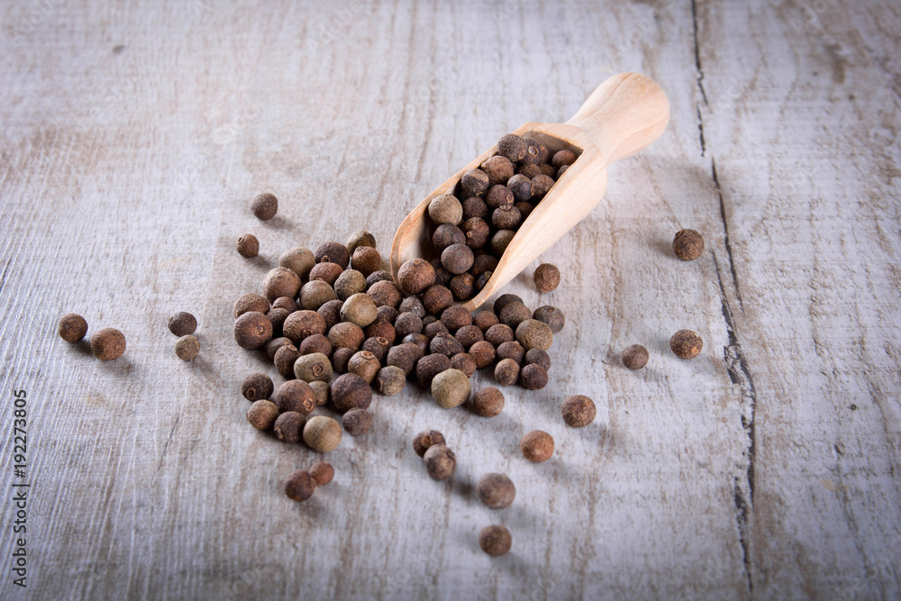 Pepper peas in a wooden spoon on a wooden background. Spices are scattered on the table Pepper peas in a wooden spoon on a wooden background. Spices are scattered on the table