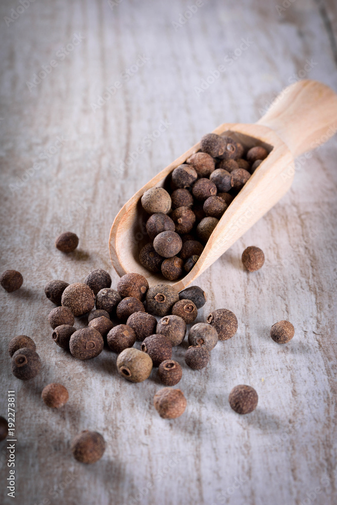 Pepper peas in a wooden spoon on a wooden background. Spices are scattered on the table Pepper peas in a wooden spoon on a wooden background. Spices are scattered on the table