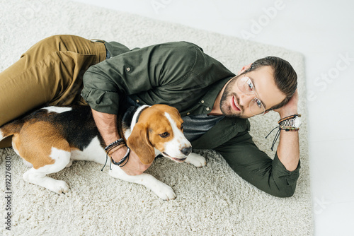 high angle view of handsome man lying on carpet with cute beagle and looking at camera