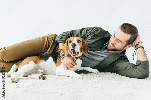 handsome man lying on carpet with cute beagle isolated on white