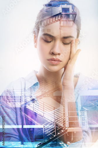 Unpleasant memories. Calm serious young woman touching her face while standing with her eyes closed and trying to remember an important piece of information