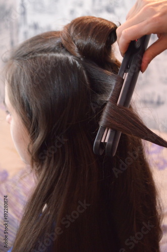 Процесс накручивания волос утюжком - красивая молодая девушка с очень длинными волосами 