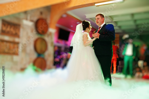 Happy young wedding couple dancing their first dance with different lights and heavy smoke in the restaurant on their wedding party.